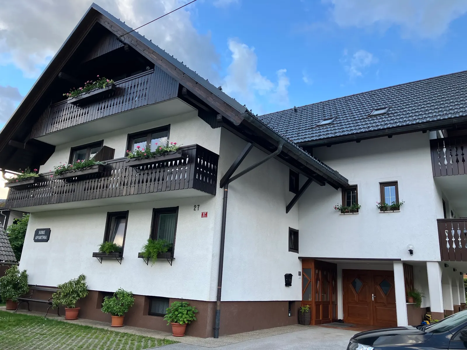 Vhod v hišo s stopnicami, rožami in napisom SOBE